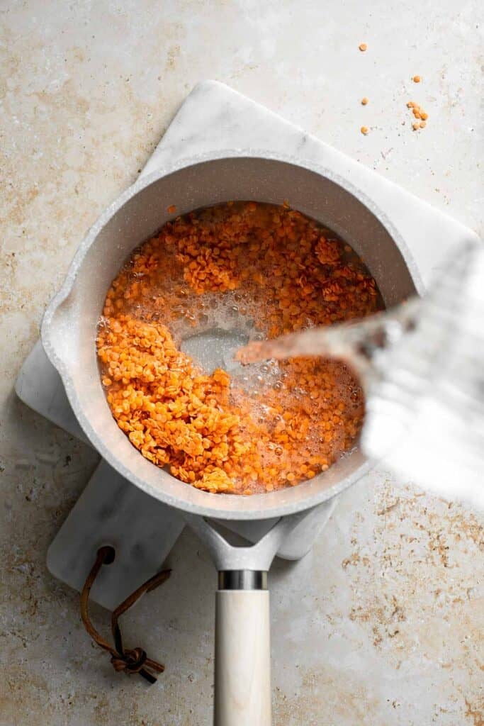 Adding water to red lentils in a saucepan.