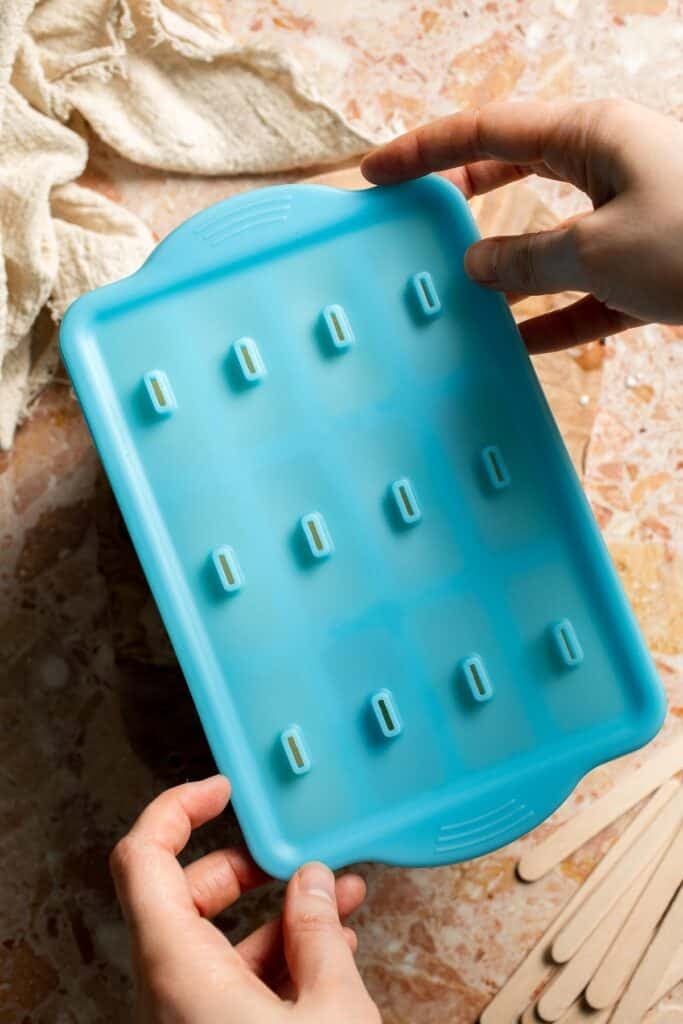 Placing the lid on a filled popsicle mold before freezing.