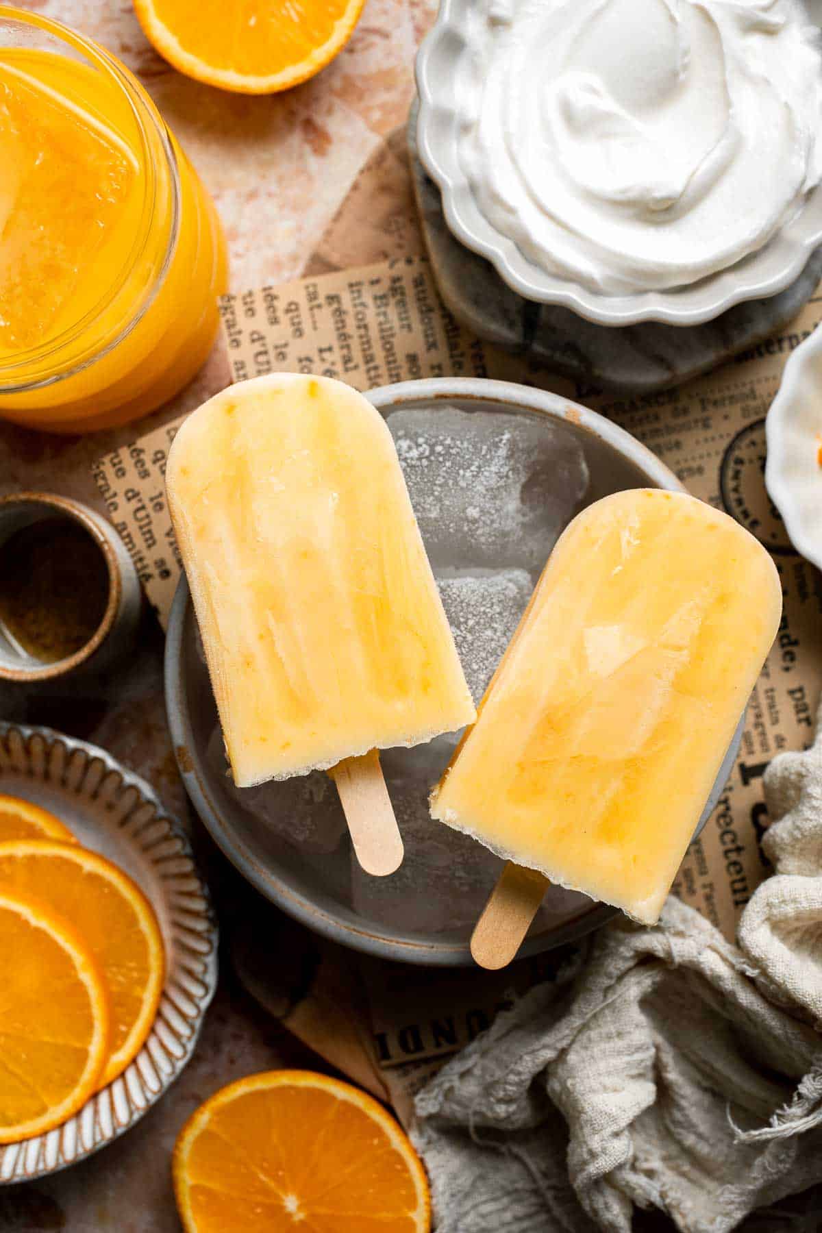 Orange Creamsicles arranged on a plate with fresh oranges and cream.