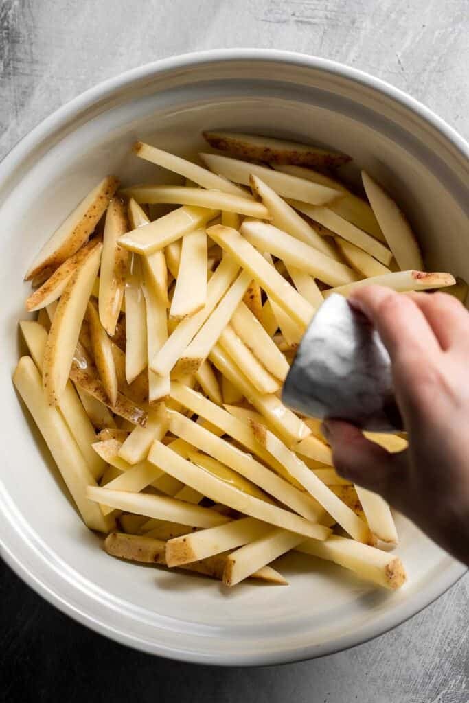 Adding olive oil to soaked potato fries before seasoning.