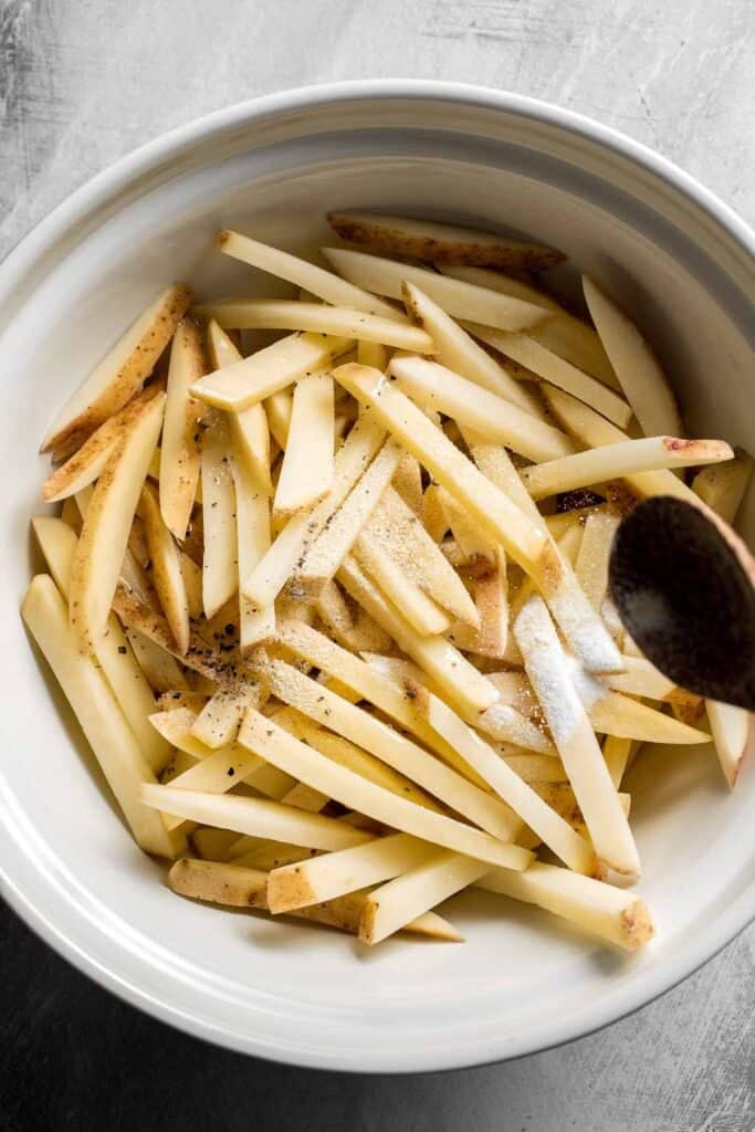 Seasoning homemade French fries with garlic powder, salt, and black pepper.