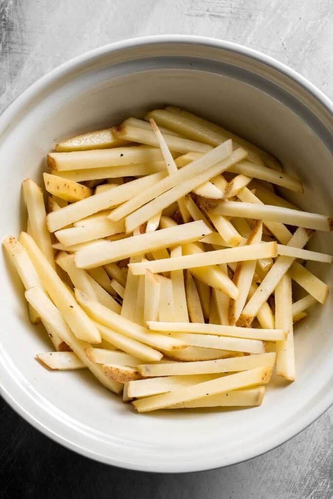 Tossed and seasoned potato fries ready for baking.