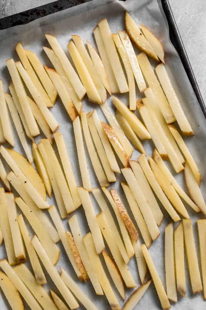 Seasoned French fries arranged in a single layer on a baking sheet.