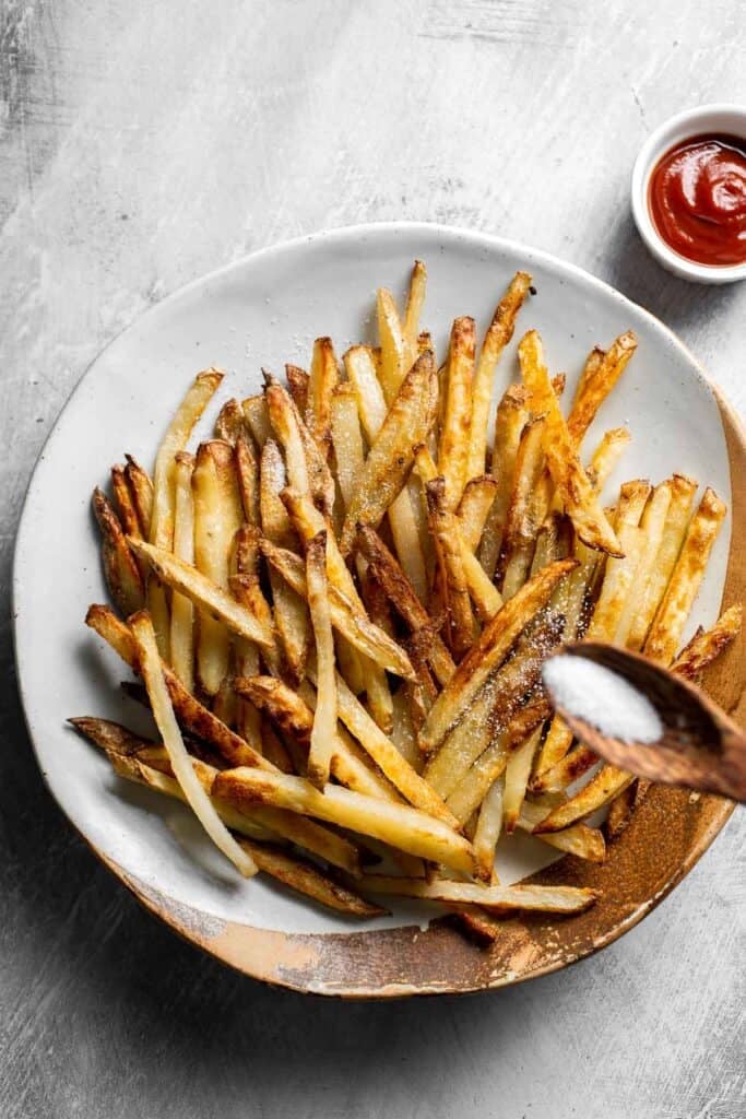Sprinkling salt over crispy oven baked french fries fresh from the oven.