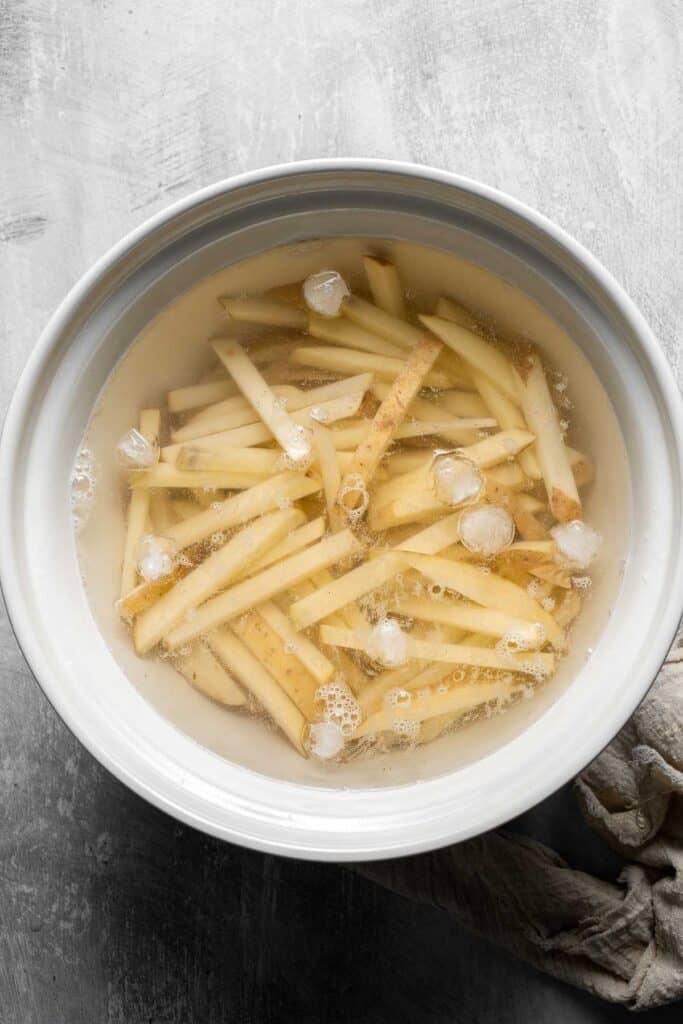 Cut potatoes soaking in cold water for crispy oven baked French fries.