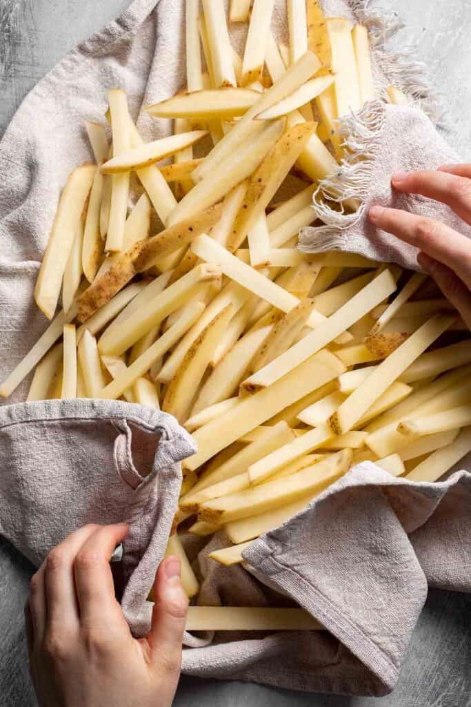 Patting soaked French fries dry with a clean kitchen towel.