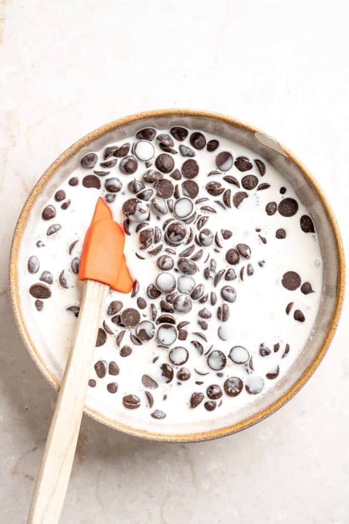 Pouring hot heavy cream over chopped semi-sweet chocolate to make chocolate ganache.