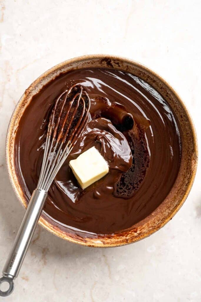 Whisking butter into melted chocolate ganache until smooth and glossy.