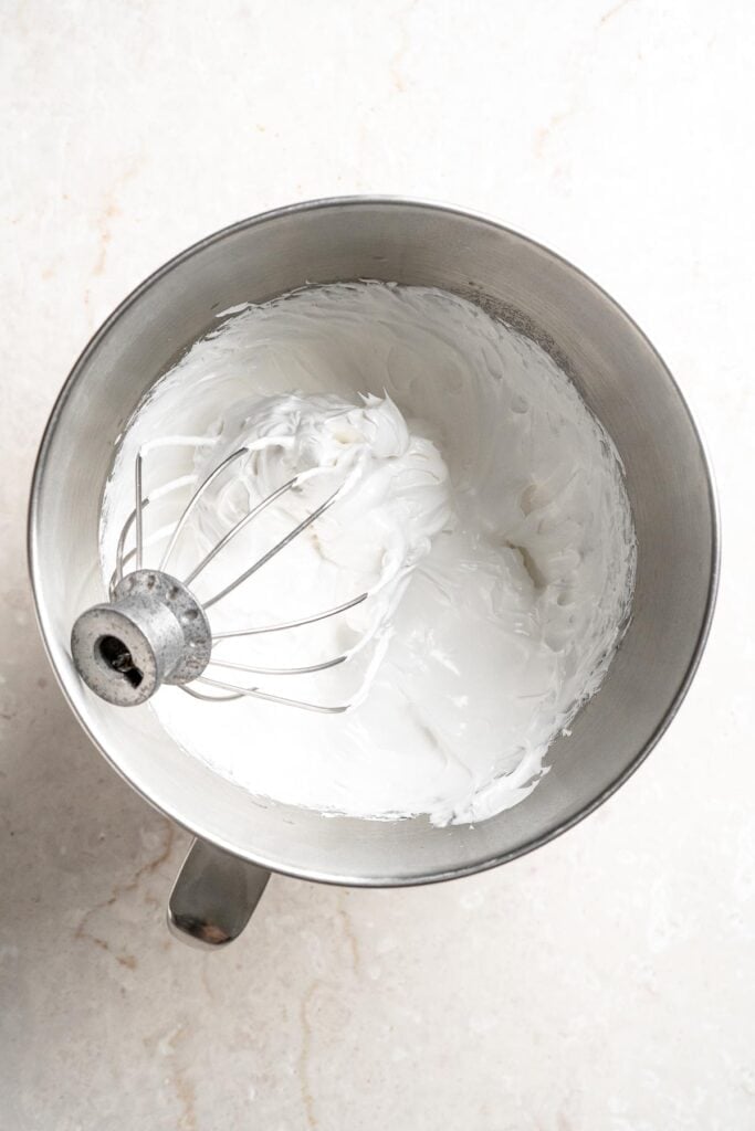 Whipping the homemade marshmallow topping in a stand mixer until thick and glossy.