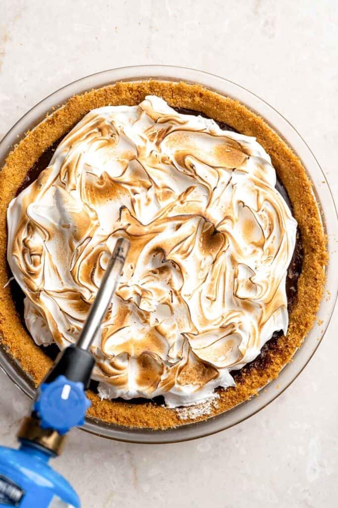 Toasting the marshmallow topping on S'mores Pie with a kitchen torch until golden brown.