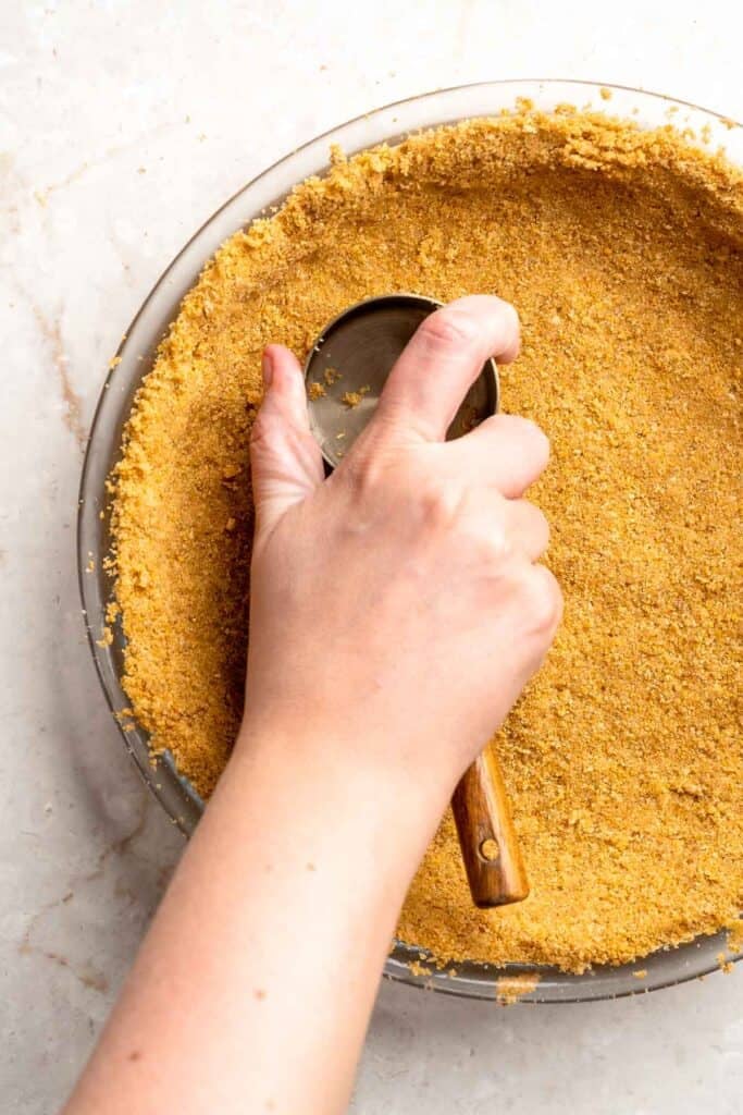 Pressing the graham cracker crust firmly into the bottom and sides of a pie dish.