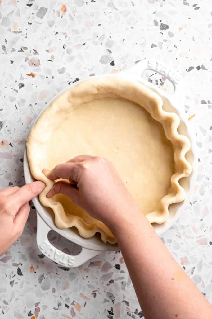 A hand crimping the edges of a pie crust