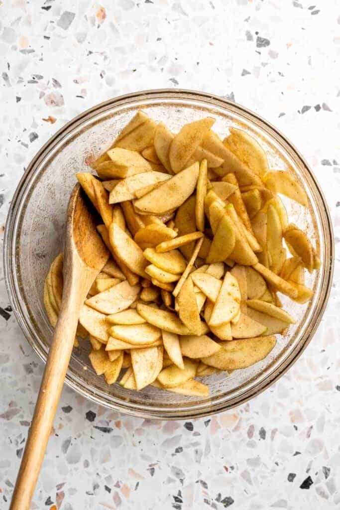 Sliced apples tossed with sugar and spices in a glass bowl