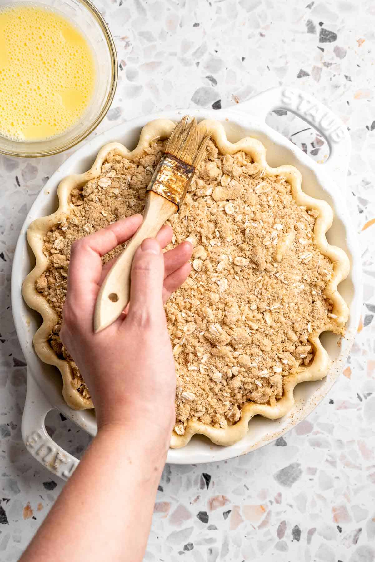 Egg wash being brushed onto the edges of an unbaked apple crumble pie