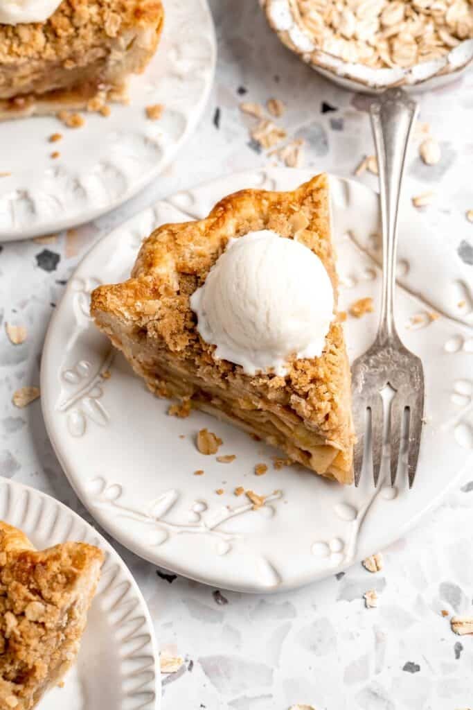 A slice of apple crumble pie topped with a scoop of vanilla ice cream on a plate