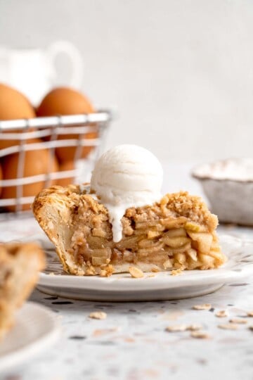 Apple crumble pie slice served with a scoop of vanilla ice cream and golden oat crumble topping.