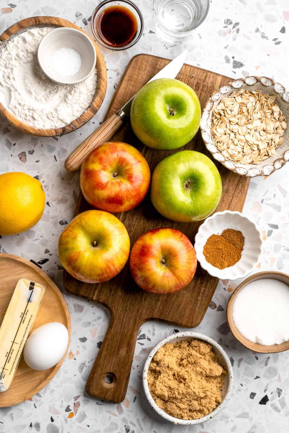 Ingredients for apple crumble pie including apples, flour, butter, and spices arranged on a wooden board