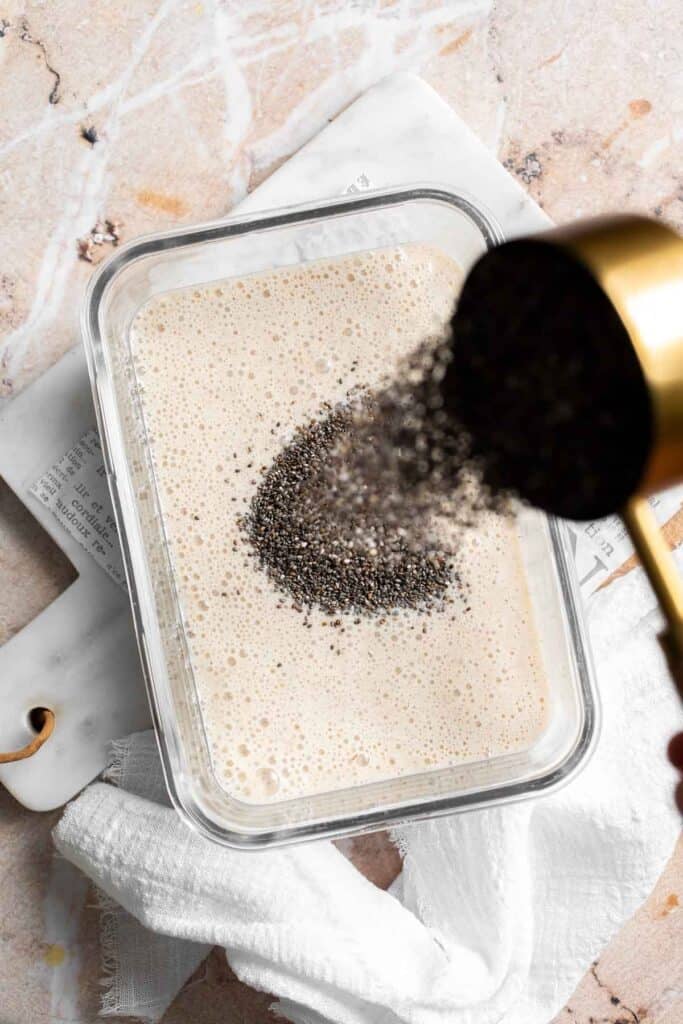 Chia seeds being poured into a container of blended banana mixture