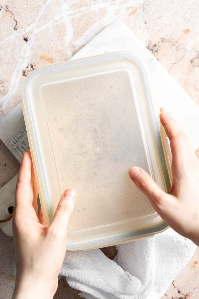 A glass container of chia pudding mixture being covered with a lid