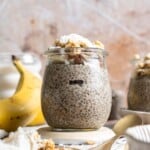Banana chia pudding in a jar topped with granola, nuts, banana slices, and shredded coconut