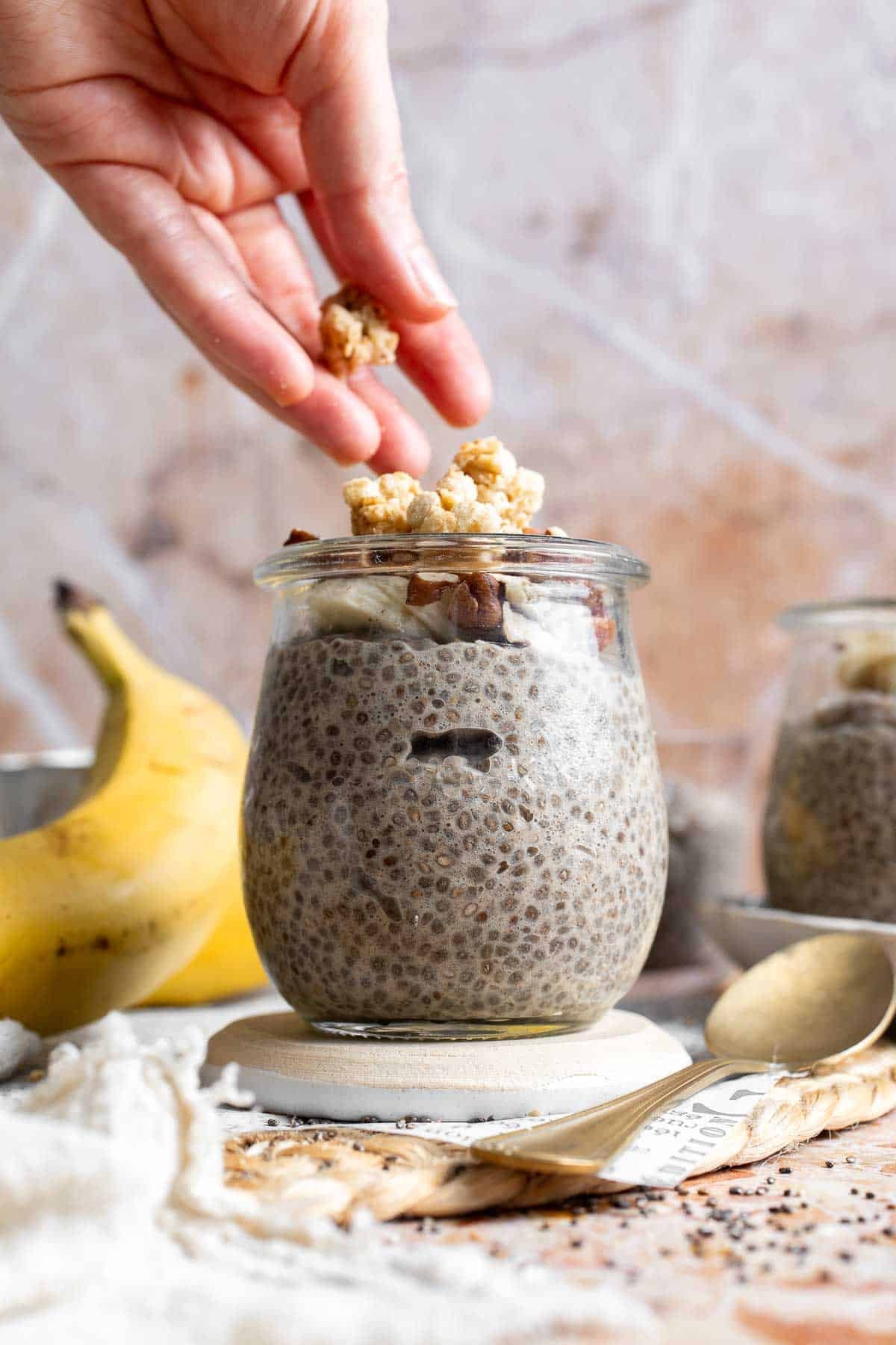 A hand adding granola to the top of banana chia pudding