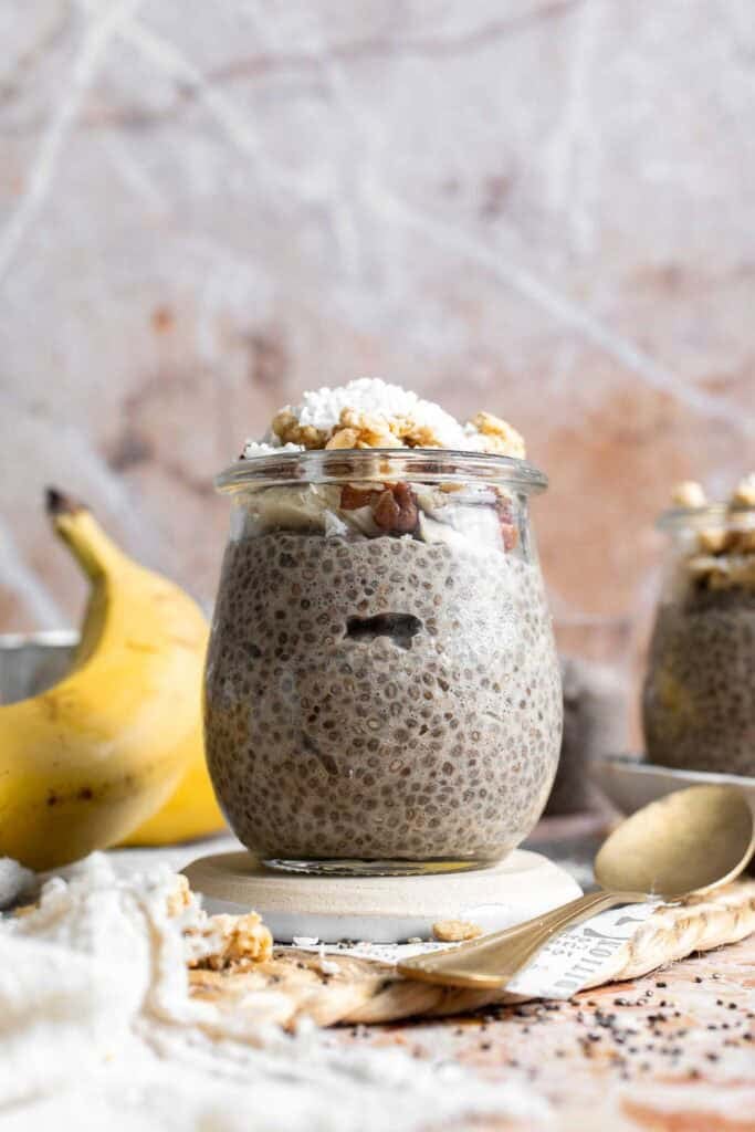 Banana chia pudding in a jar topped with granola, nuts, banana slices, and shredded coconut