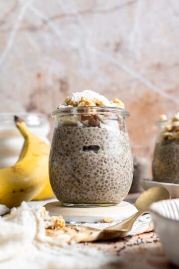 Banana chia pudding in a jar topped with granola, nuts, banana slices, and shredded coconut