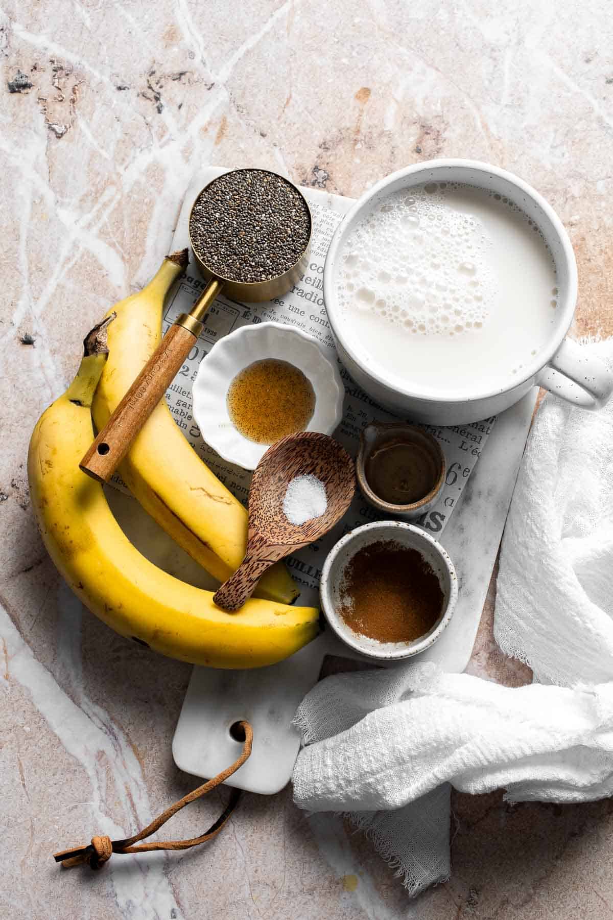 Ingredients for banana chia pudding including bananas, chia seeds, milk, and spices arranged on a table