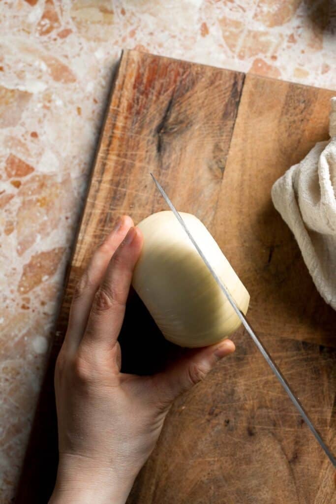 Slicing a peeled sweet onion into thick rounds.