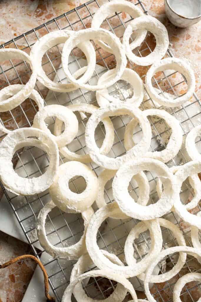 Floured onion rings arranged on a wire rack.
