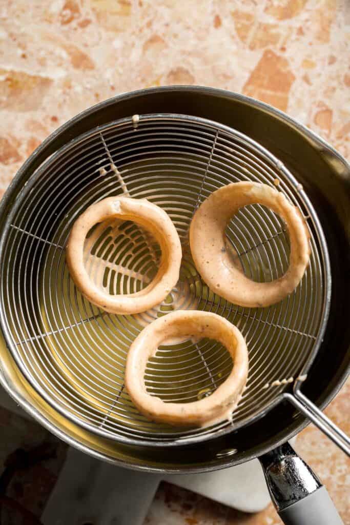 Beer battered onion rings being lowered into hot oil.