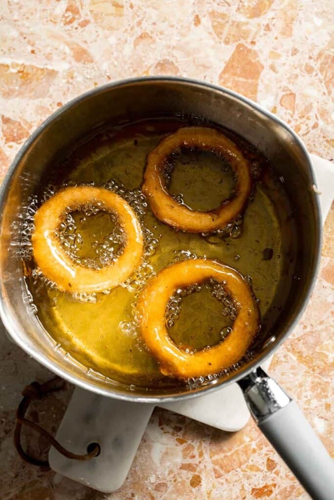 Beer battered onion rings turning golden brown while frying.