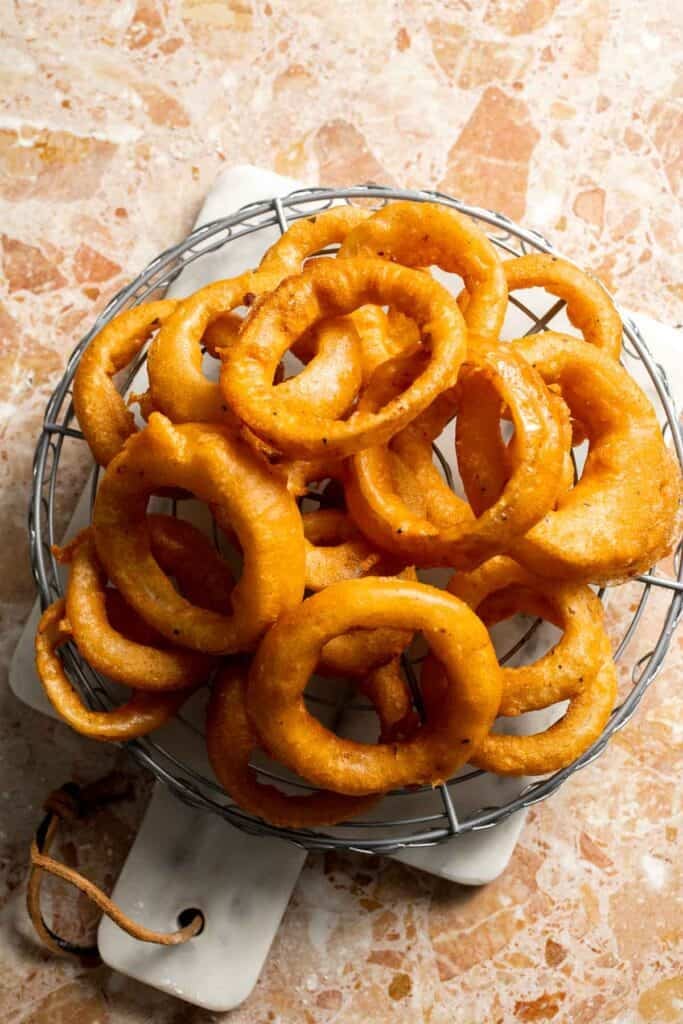 Freshly fried Beer Battered Onion Rings cooling on a wire rack.