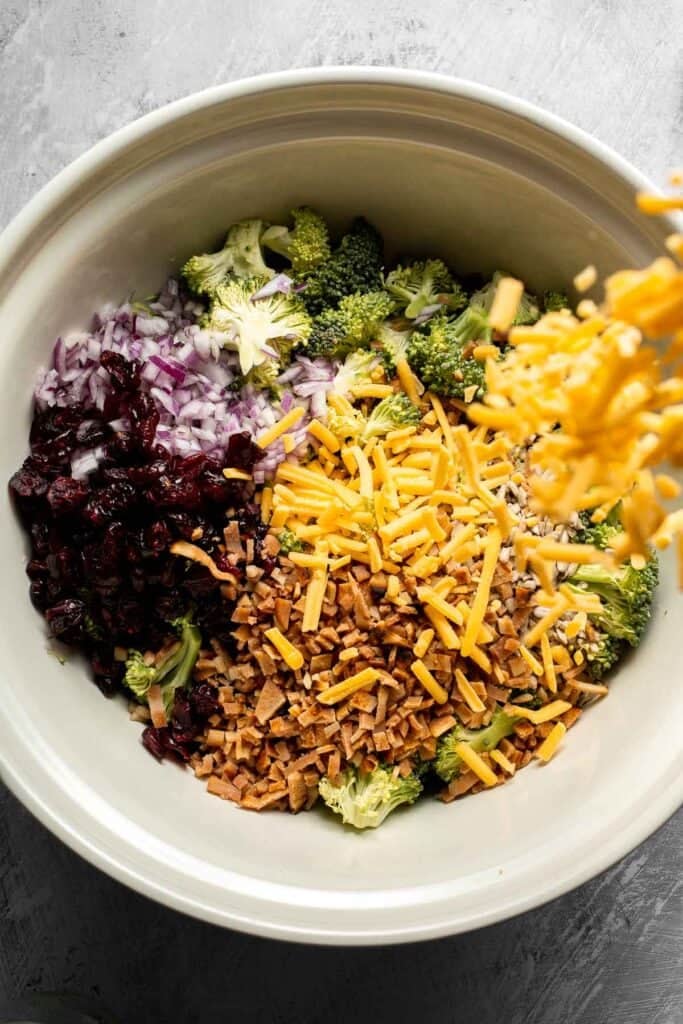 Adding shredded cheddar cheese to the broccoli salad.