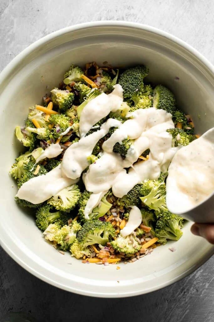 Pouring the creamy dressing over the broccoli salad.