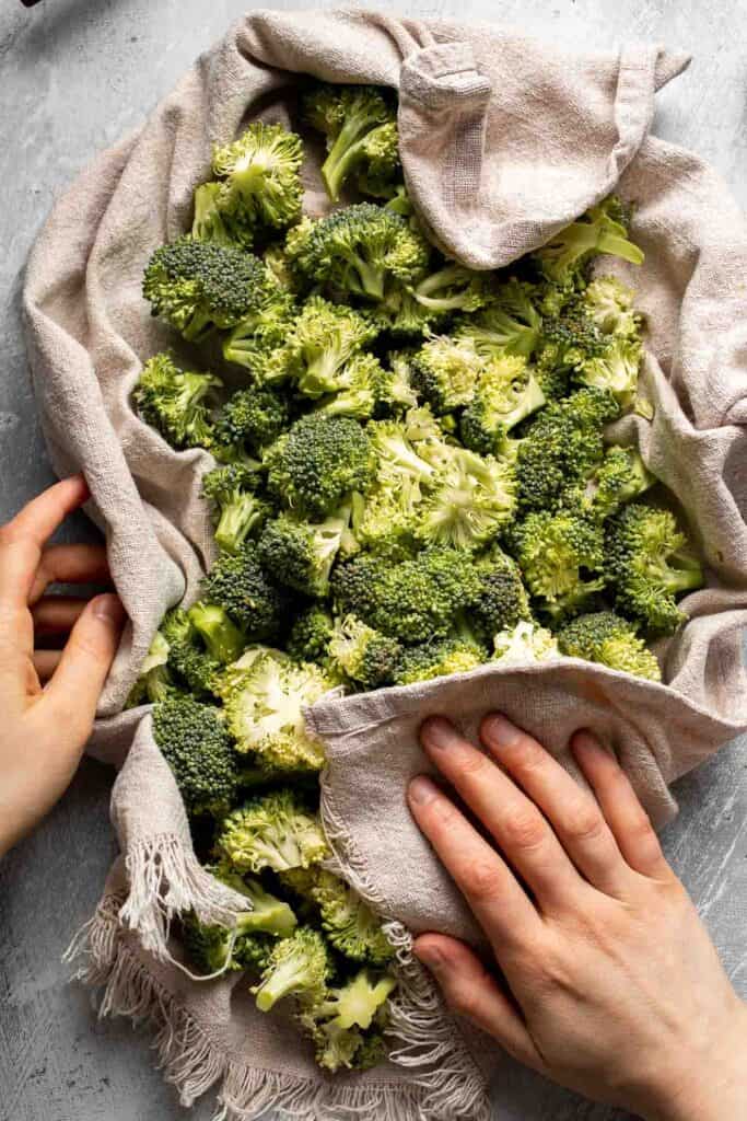 Drying fresh broccoli florets with a clean kitchen towel.