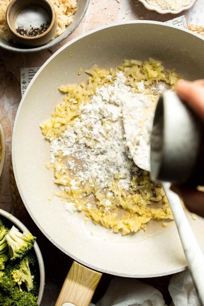 Flour being stirred into sautéed shallot and garlic to make a roux