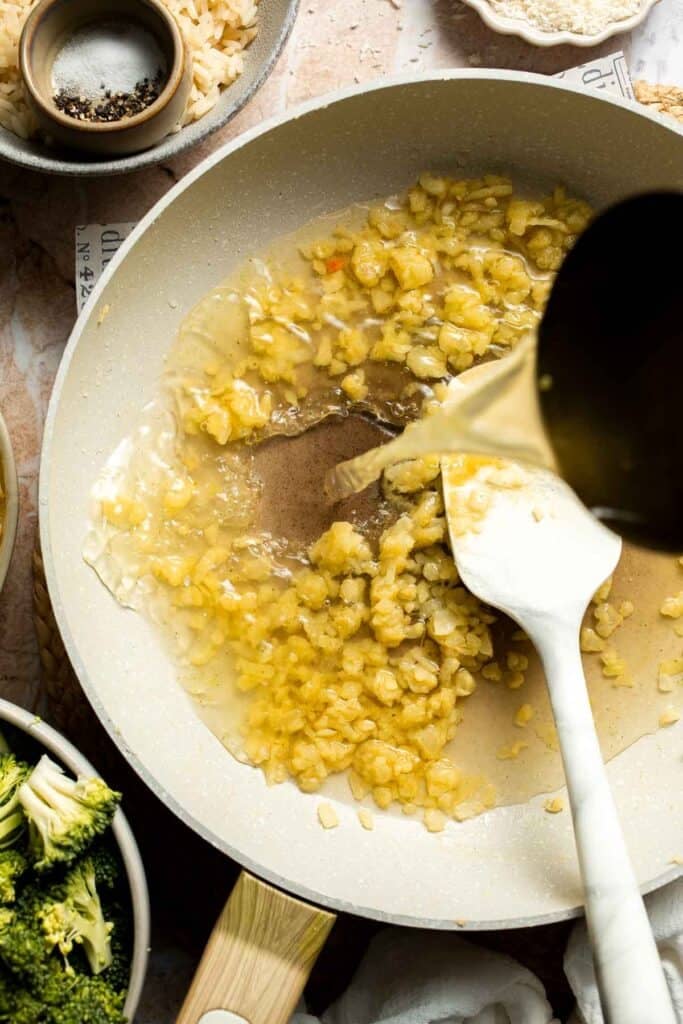 Chicken broth being poured into a skillet with a roux
