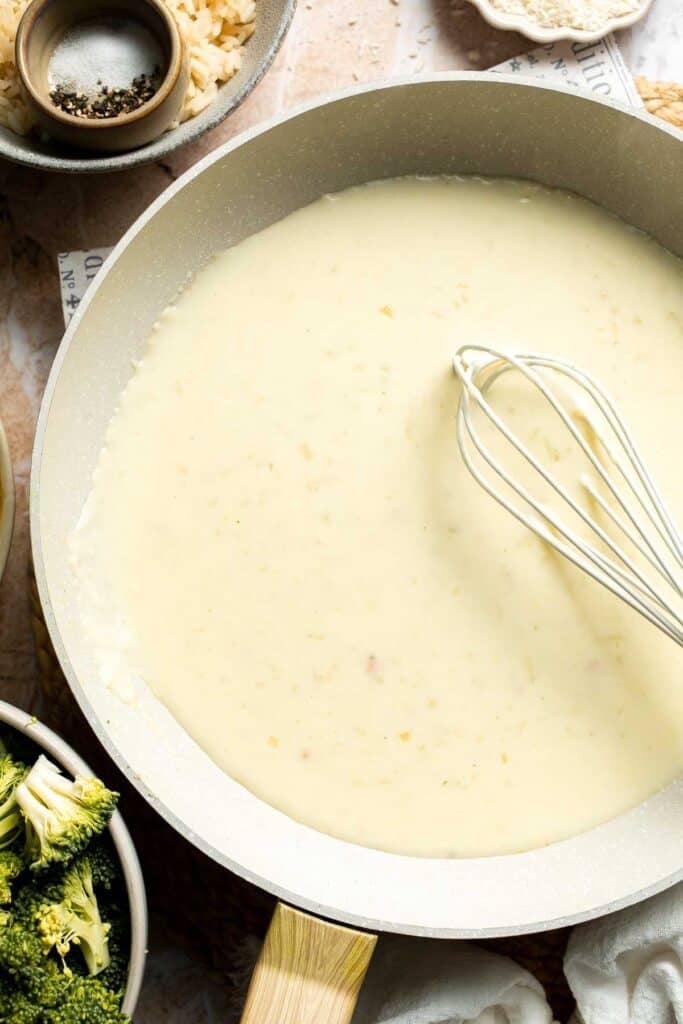 A creamy sauce being whisked smooth in a skillet
