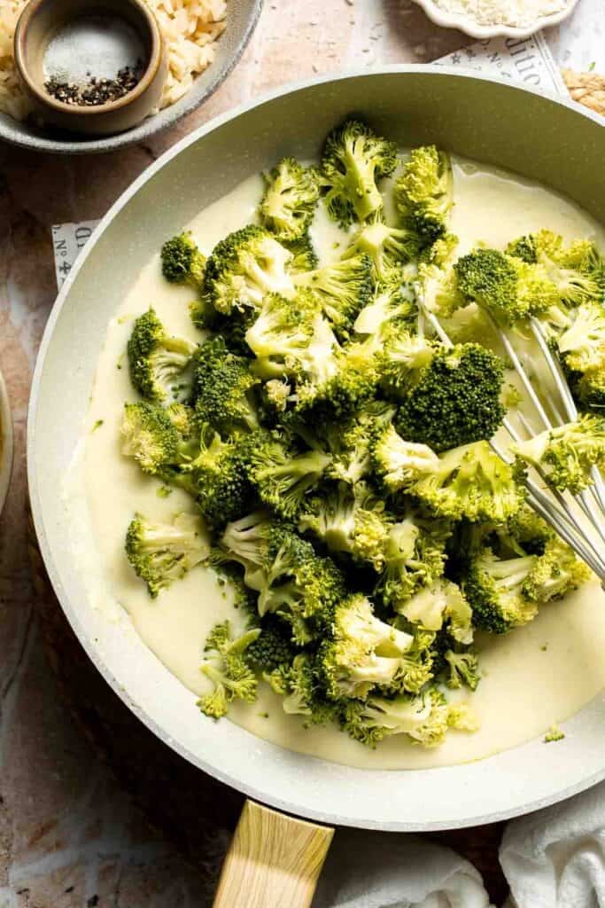 Broccoli florets added to a creamy sauce in a skillet