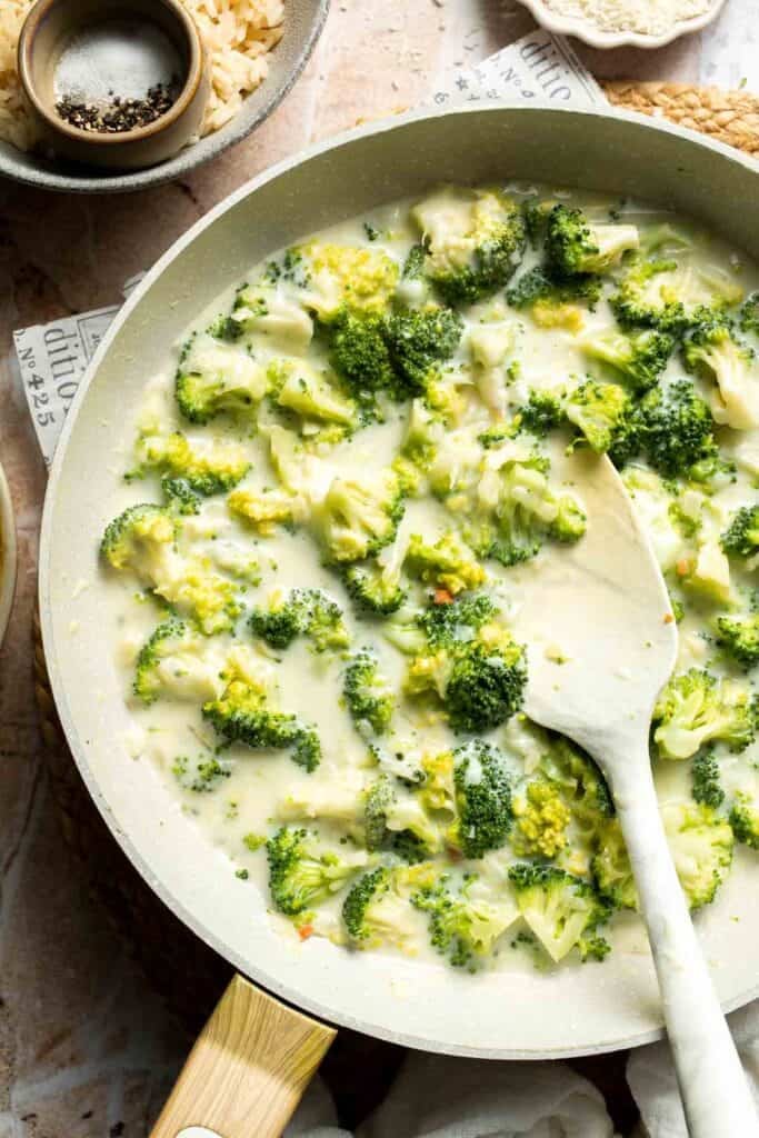 Broccoli florets stirred into a creamy sauce in a skillet