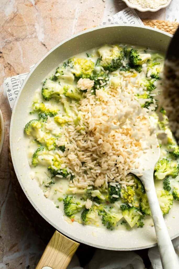 Rice being stirred into broccoli and cheese sauce in a skillet