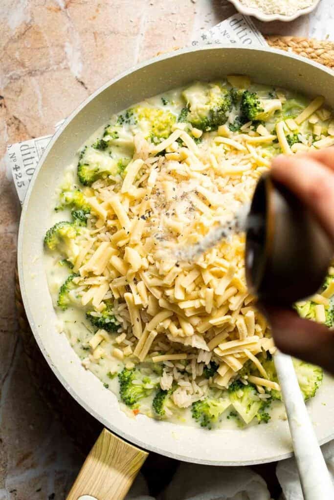 Salt and pepper being sprinkled over broccoli rice casserole filling in a skillet