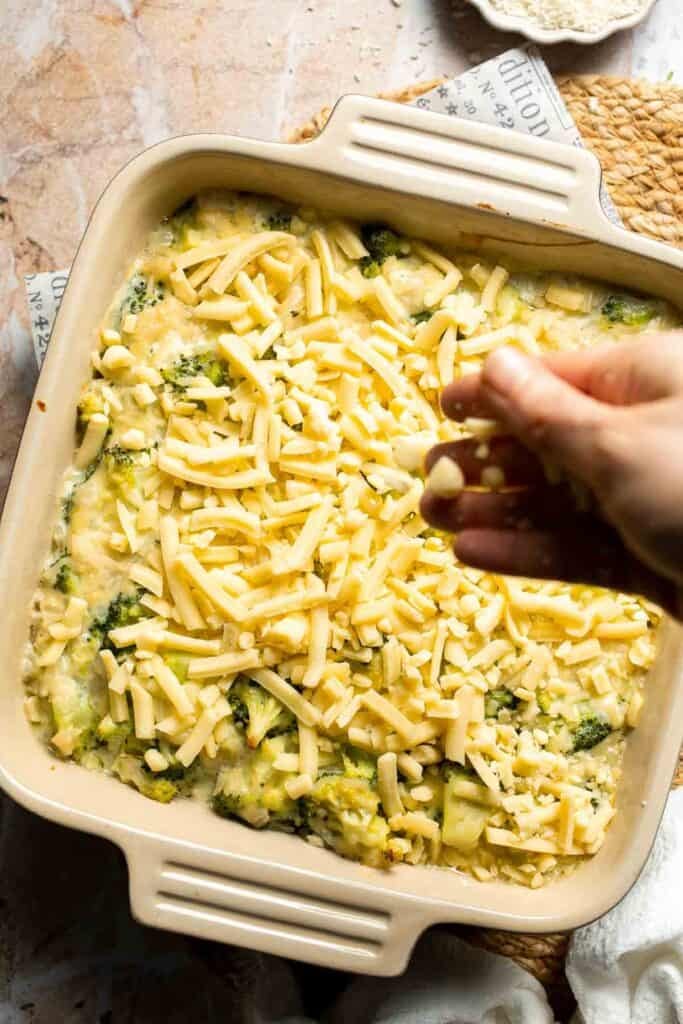 Shredded cheddar cheese being sprinkled over partially baked broccoli rice casserole