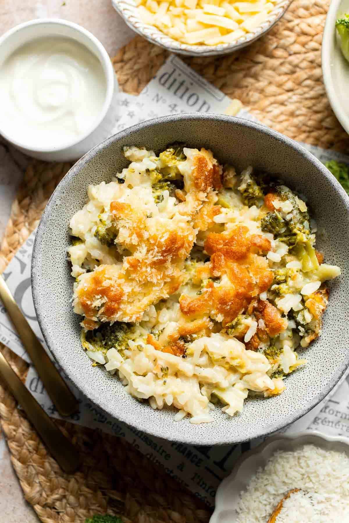 A serving of cheesy broccoli rice casserole scooped into a bowl next to the baking dish