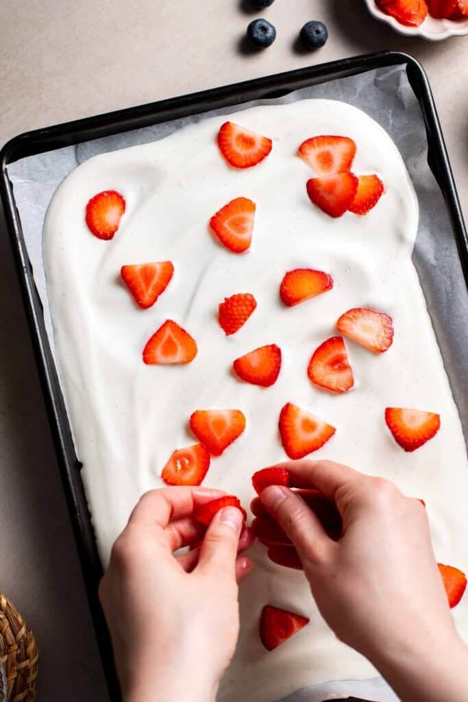 Sliced strawberries being arranged on top of spread yogurt on a baking tray