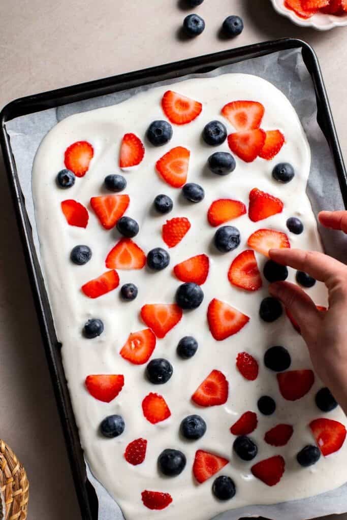Blueberries and sliced strawberries scattered over yogurt on a baking tray