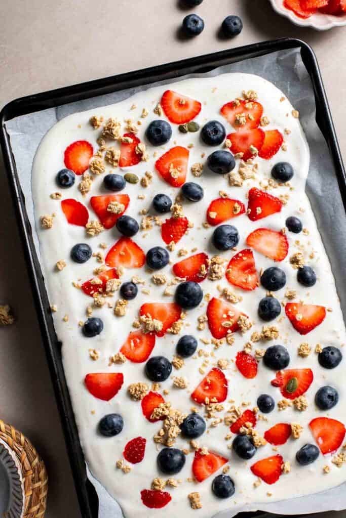 Strawberries, blueberries, and granola scattered over a tray of yogurt
