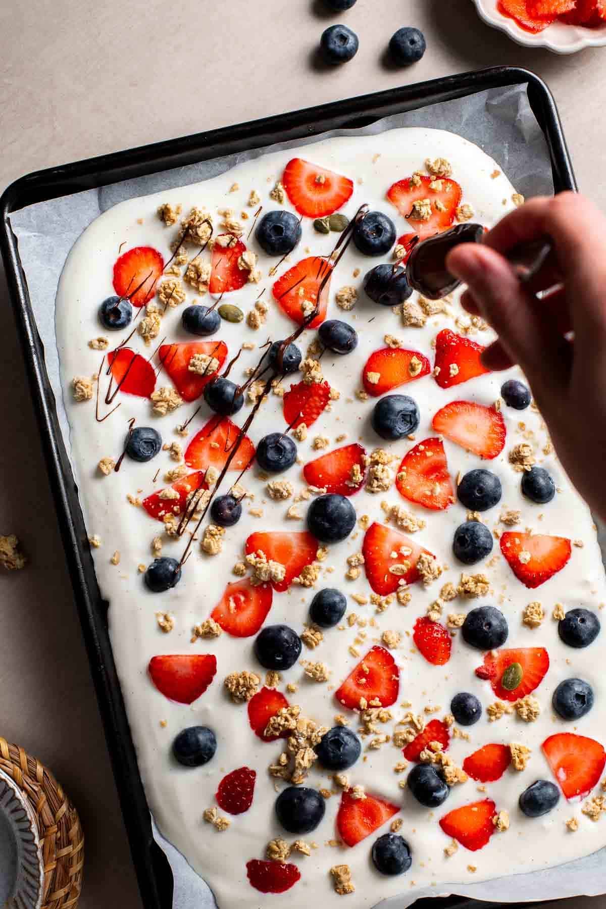 Melted chocolate drizzled over yogurt bark topped with berries and granola