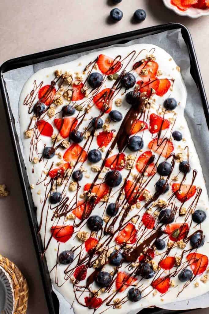 Overhead view of frozen yogurt bark drizzled with chocolate before freezing
